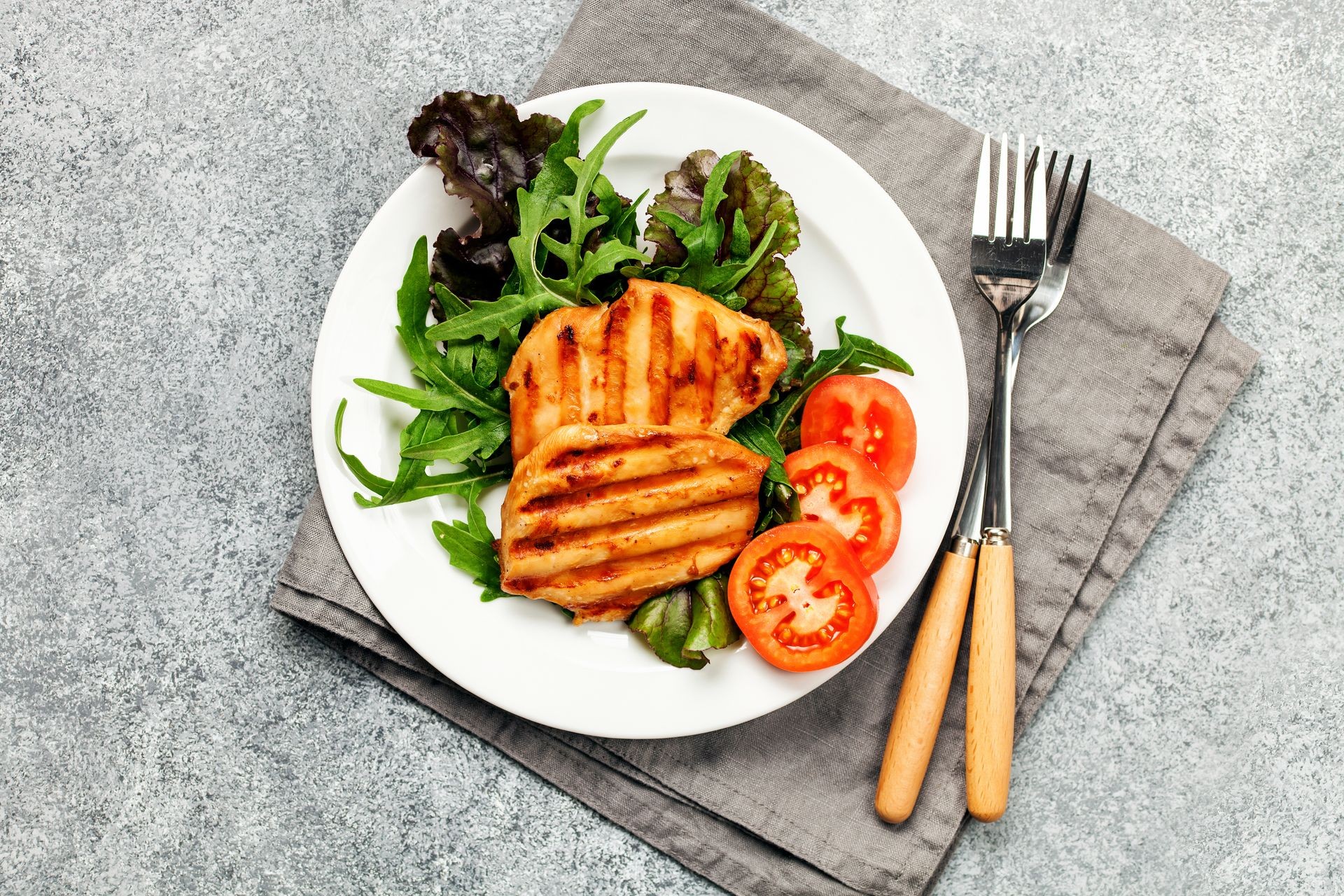 Grilled chicken breast. Fried chicken fillet and fresh vegetable salad of tomatoes, mangold and arugula leaves. Chicken meat salad. Healthy food. Flat lay. Top view. Gray background